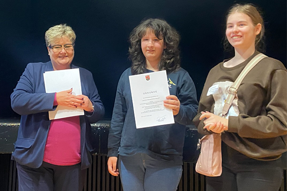 Links Staatssekretärin Bettina Brück, rechts daneben die Schülerinnen Karina Meyer und Lilly Heidebrecht mit einer Urkunde 
