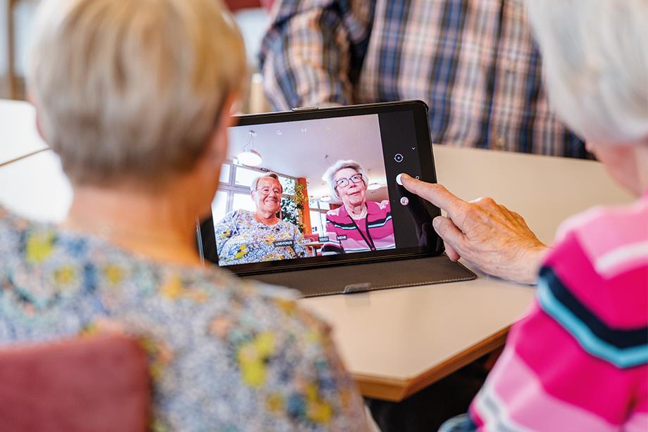 Zwei Seniorinnen sitzen gemeinsam vor einem Tablet und machen ein Selfie (Foto von sich selbst).
