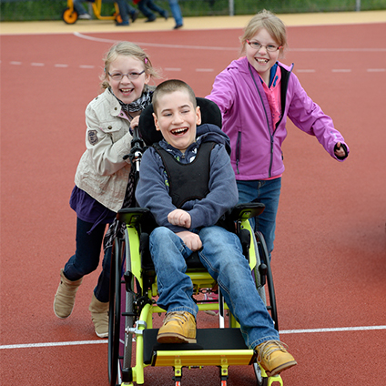 Eine Gruppe von Kindern steht oder läuft auf einem Platz vor der Schule. 